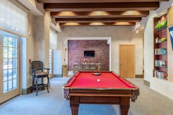 A pool table is in the middle of a room with a chair and a window